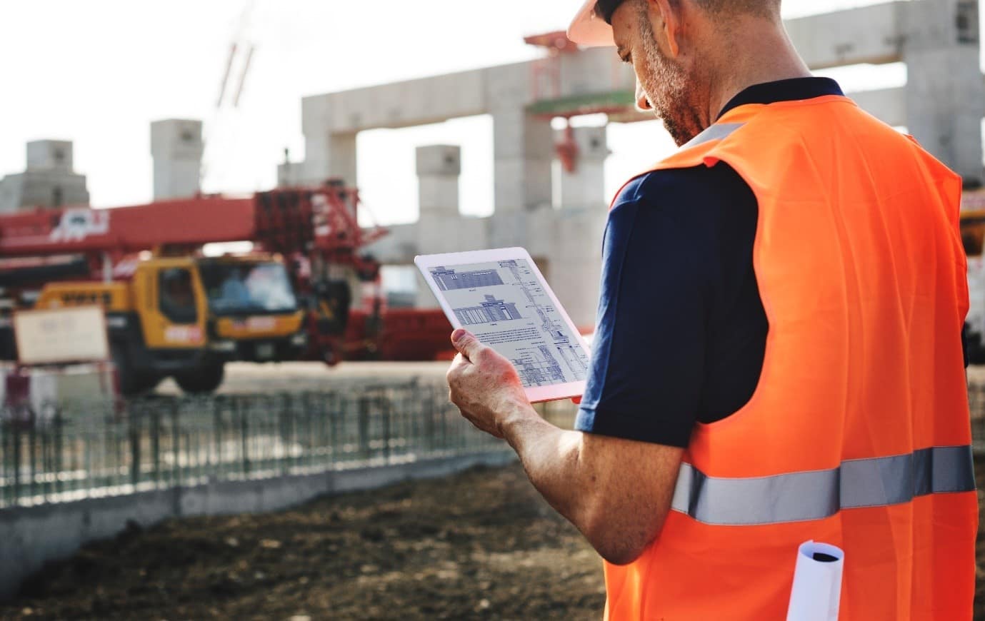 A construction worker looking at plans, stood in front of a building foundation