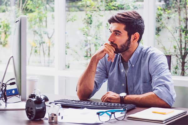 A Contractor’s Guide to IR35 - Part 1- Contractor in thought sat at desk, looking at computer screen.