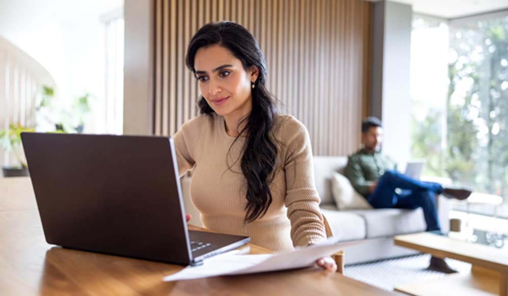 A self-employed professional working from home, sat at a table with a computer and some paperwork