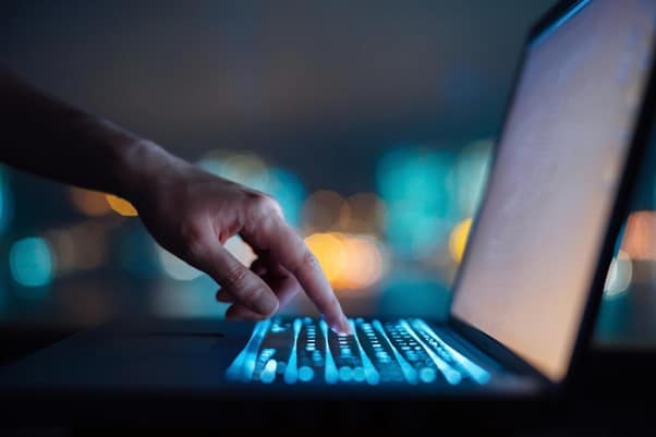 A side view of someone typing on a lit up laptop
