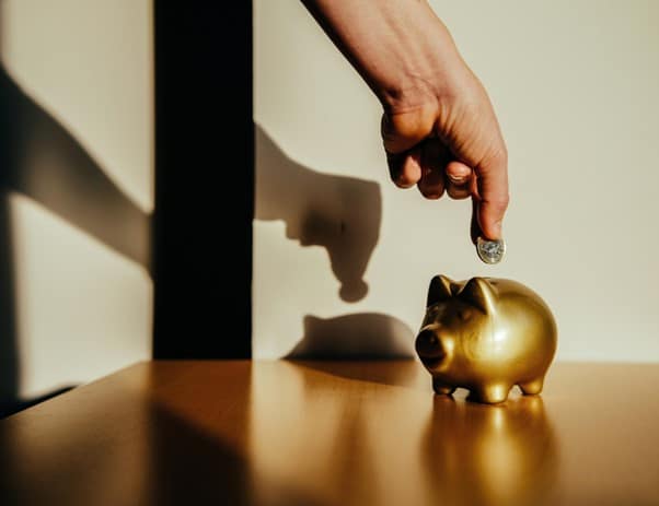A hand putting a coin into a golden piggy bank
