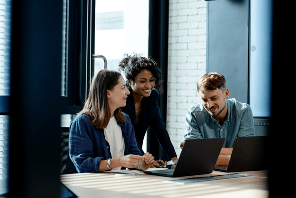 3 professionals gathered around a computer whilst smiling