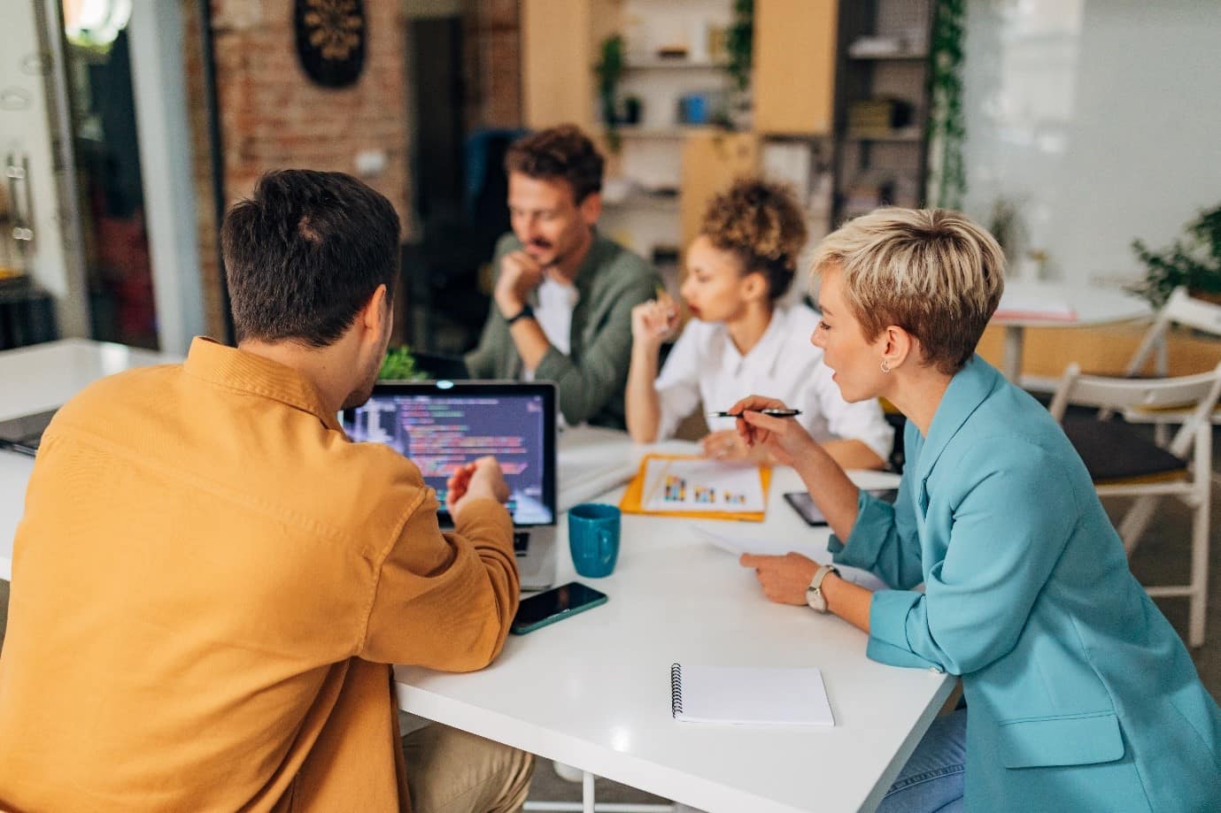 Four people sat around around a table looking at at information on a computer and printed paper