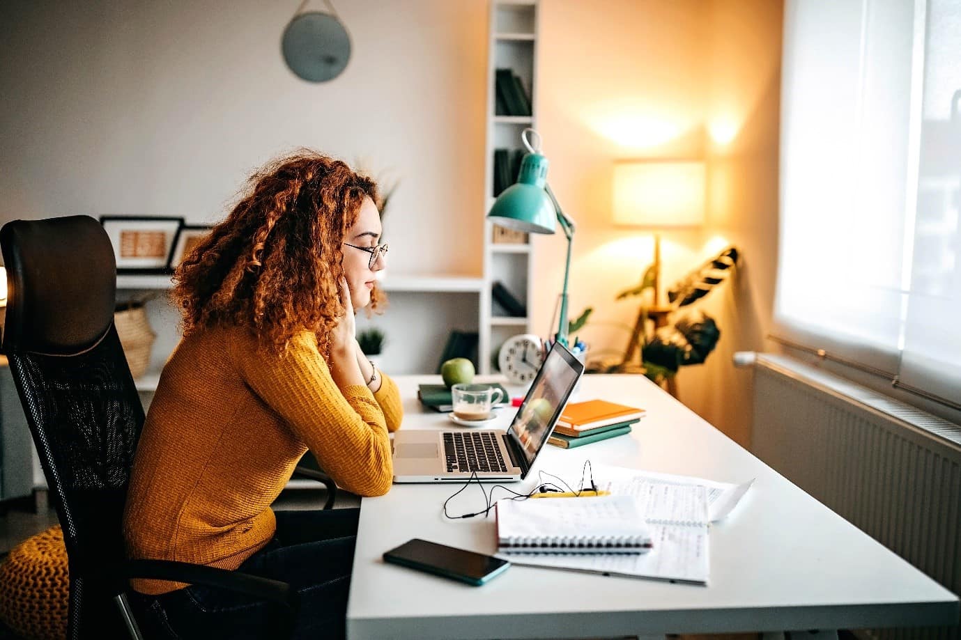 A contractor sat infront of a desk with a computer and an array of paperwork, with a bright lamp in the background