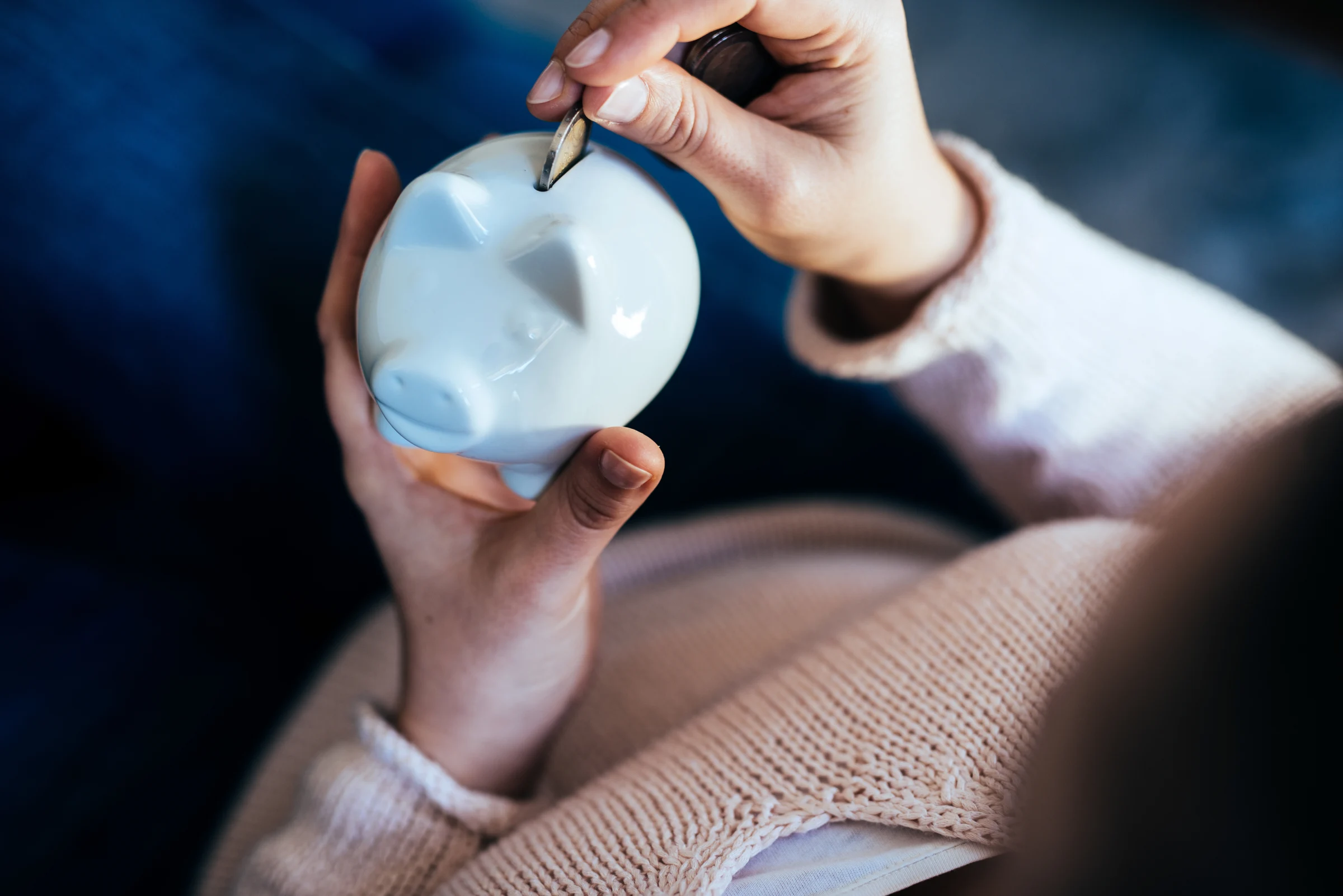 Someone holding a white piggy bank, with one hand placing a coin into it
