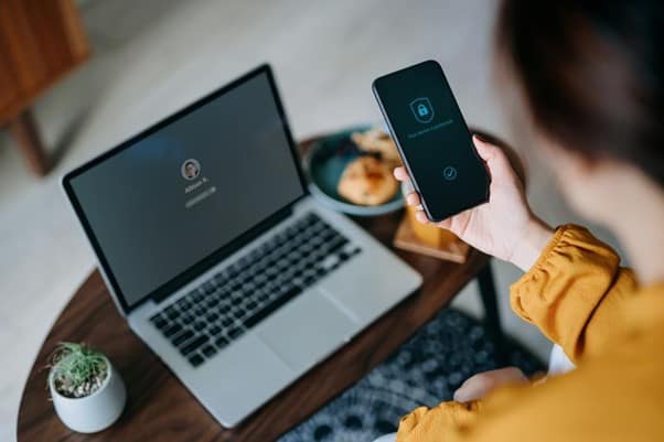 Someone holding their phone which shows an authenticator app as they try to log in to a computer