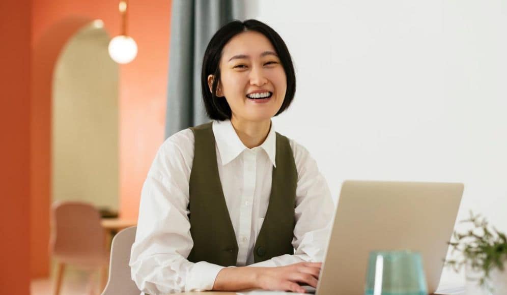 Happy businesswoman sitting at desk with laptop in office
