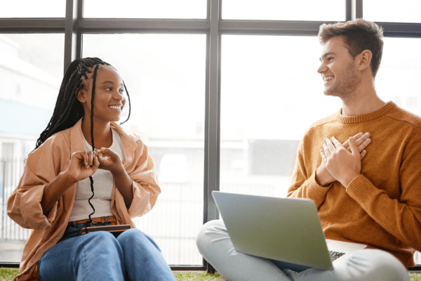 Two young people sat having a conversation, with a computer on one of their laps