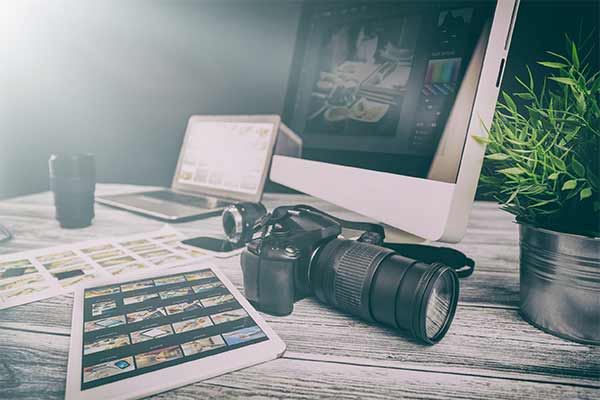 Guide to photographers insurance - Camera, Apple iMac, laptop and printed shots on a photographers desk.