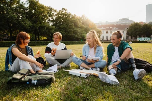 A group of young adults sat on a field with school paperwork, laughing