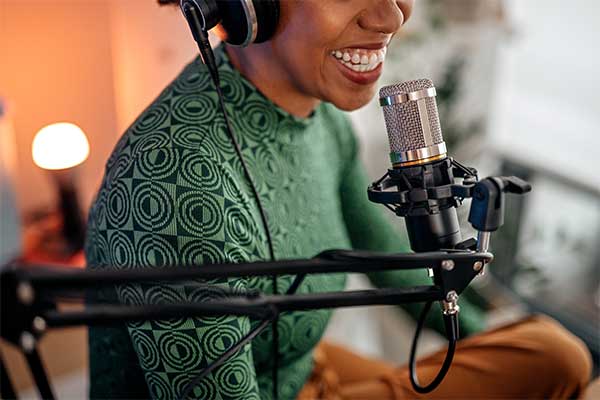 A small business owner smiling as she creates her own podcast and speaks into a microphone.