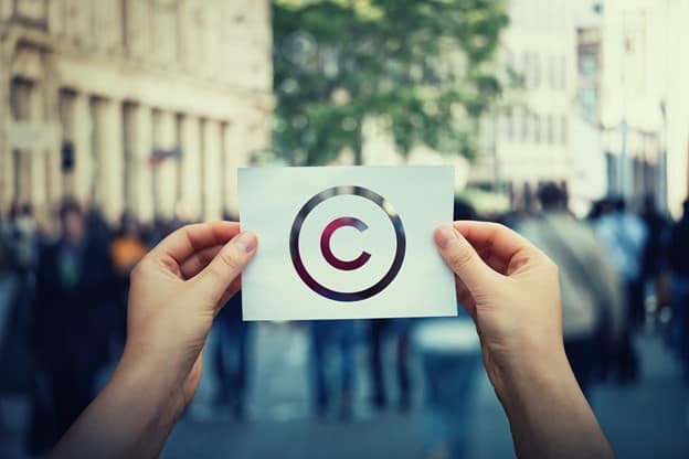 A pair of hands holding up a piece of paper representing a copyright symbol