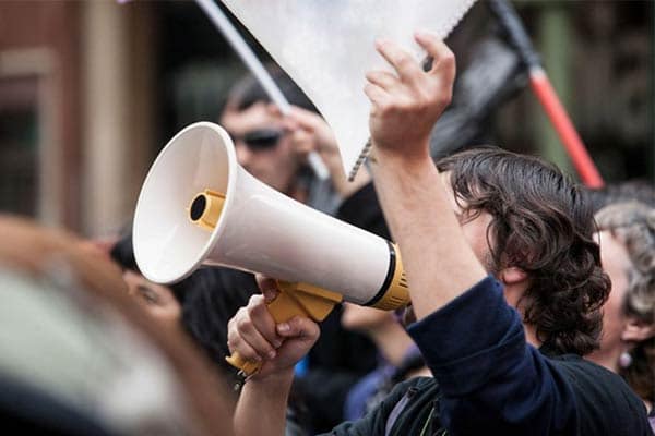 A man taking part in an industrial action, holding a megaphone and notepad.