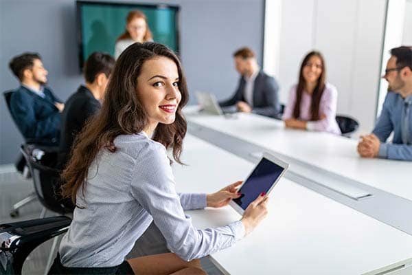 A business owner sat in a meeting room with her employees, working from an iPad.