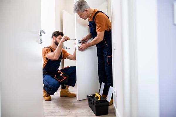 A locksmith and his apprentice changing the lock on a door. 