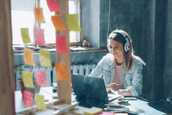 A person sat at a desk on a laptop, with lots of pink, orange and yellow post-it notes
