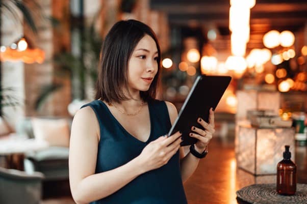 A lady stood up, concentrating on the electronic tablet screen she is holding