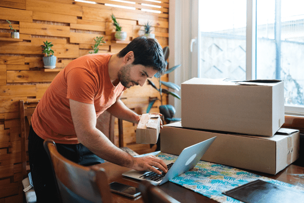 A small-business owner on their computer whilst packing cardboard boxes