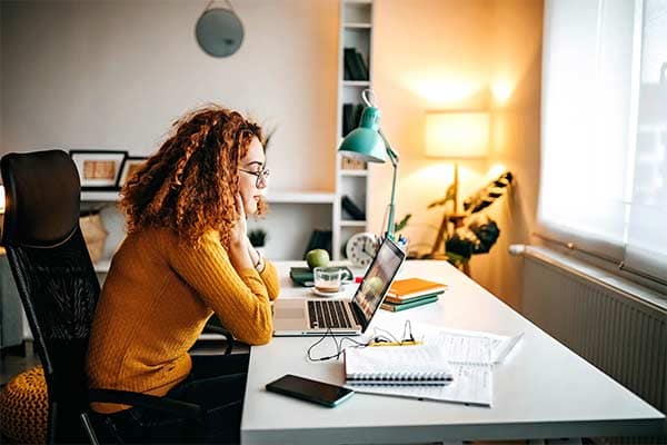 A woman working from home, sat at her desk looking at her laptop.