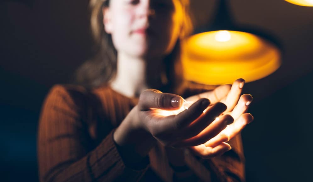 Someone stood infront of a light, holding their palms out which are also holding a light