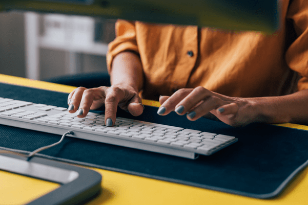 A view of some hands typing on a keyboard, below a computer