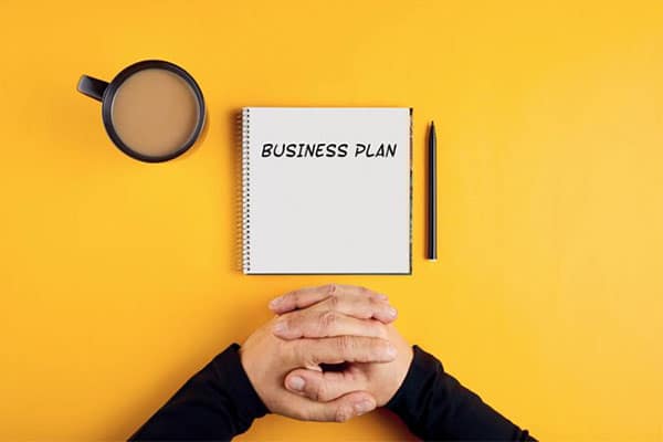 The hands of a businessman in front of a spiral notebook containing business plan ideas.