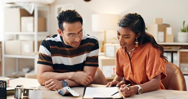 A man and women sat at a table looking at paperwork.
