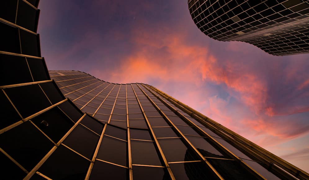 A low angle shot of a black building with a pink sky above
