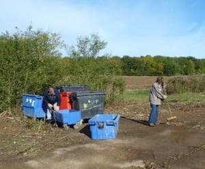 A group of volunteers sweeping up rubbish, alongside some large bins