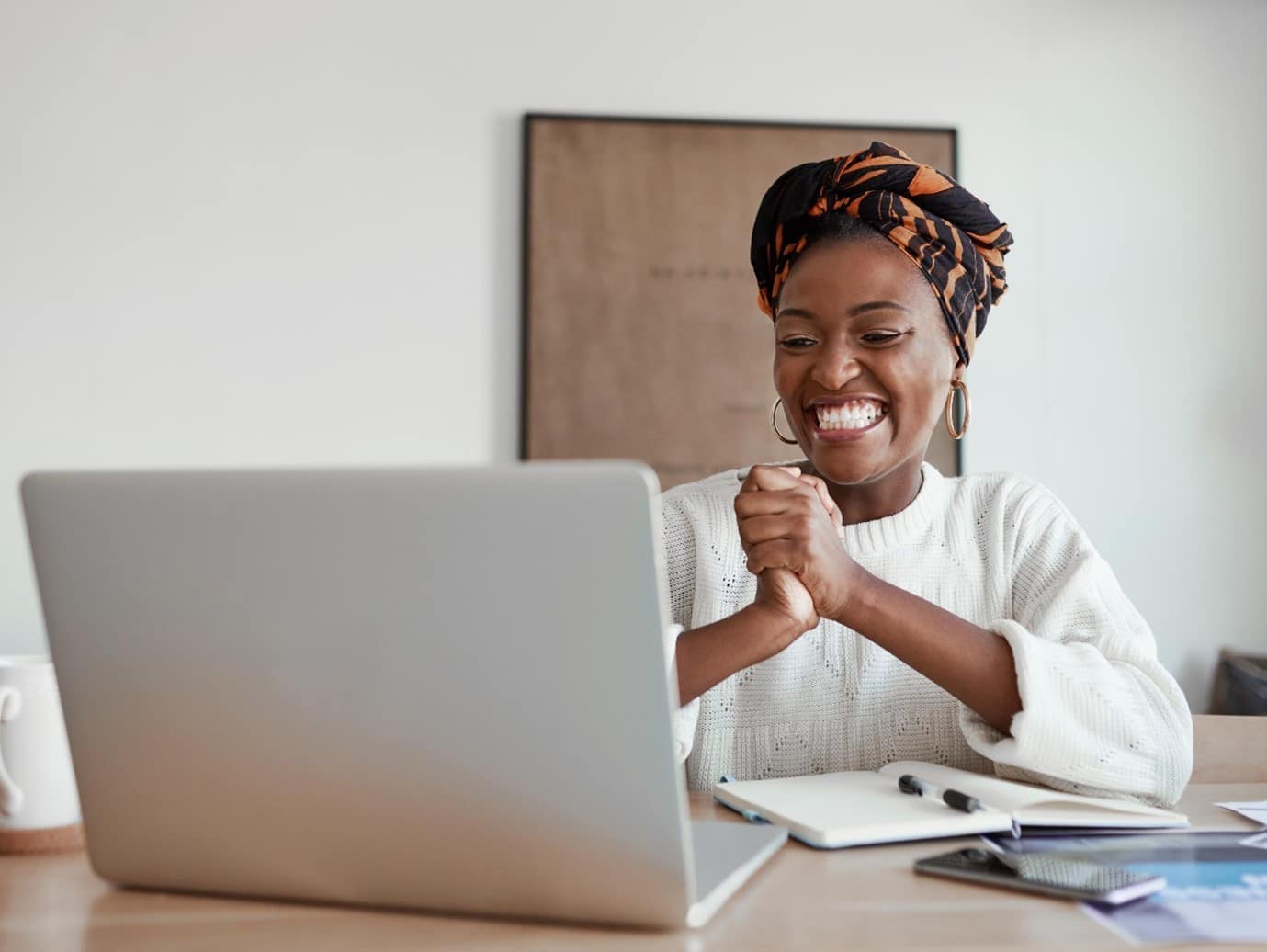 Someone smiling whilst looking at a computer screen, with a notepad and pen next to them too