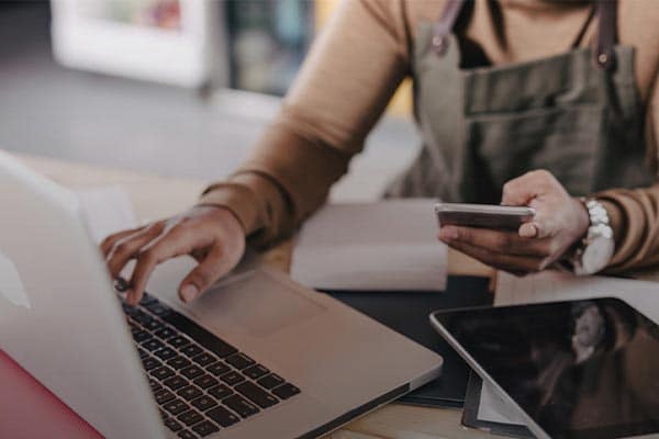 Small business owner working at laptop and holding their phone.