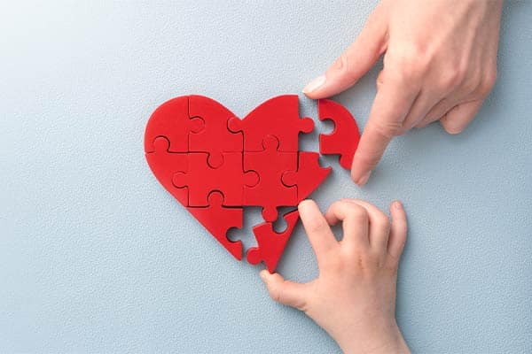 A mother and child's hand building a love heart jigsaw.