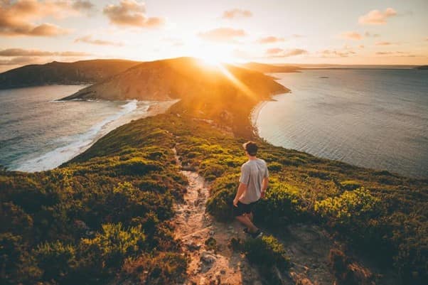 A person walking across a hill during a sunset