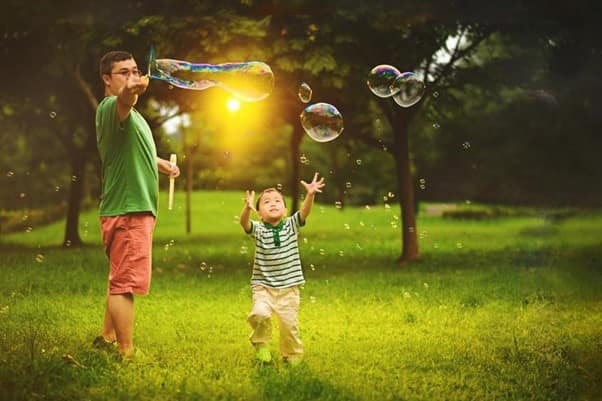 A father and son playing with bubbles in a park
