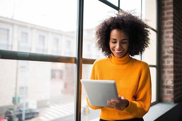 Freelancer sat on a window sill smiling as she looks down at her iPad.