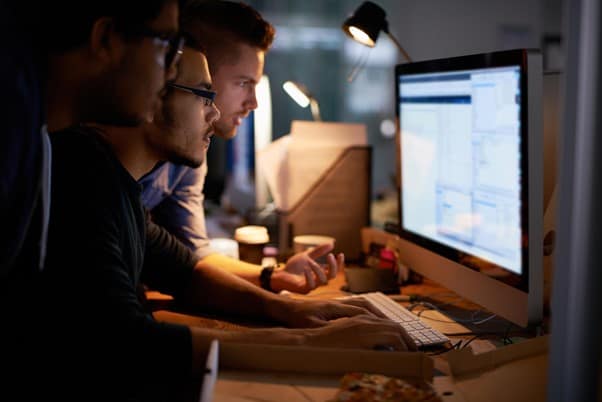 A side view of three people all looking at the same computer