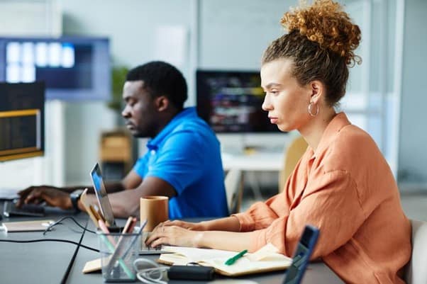 A side view of two people sat at a desk on computers