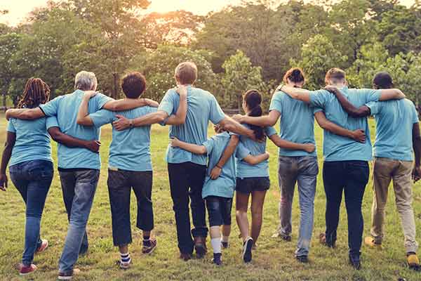 A group of volunteers wearing blue tops walking together across a field, with their arms wrapped around one another.