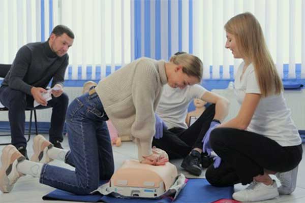 A first aider providing CPR training to an employee, who’s using a doll to practise.
