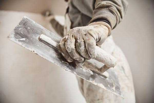 Plasterer wearing gloves and holding a finishing trowel.