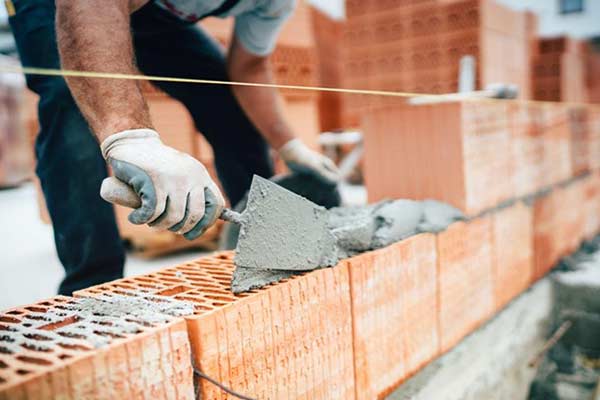 A builder applies cement and mortar while constructing a brick wall.