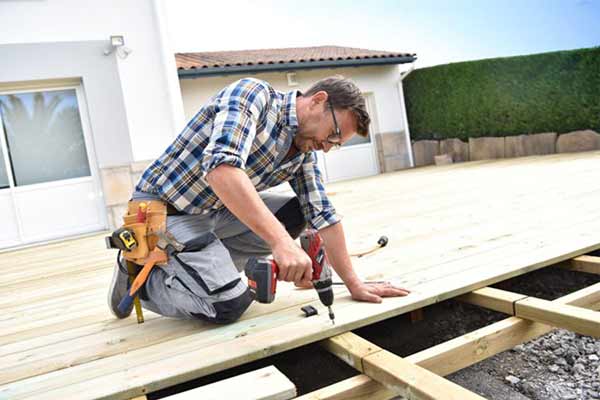A carpenter fits timber boards onto a wooden deck outside a client’s property.