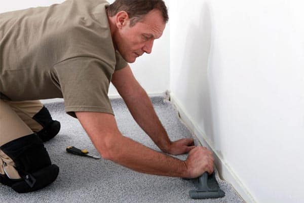 A tradesman using a carpet tucking tool to fit a carpet under a skirting board.