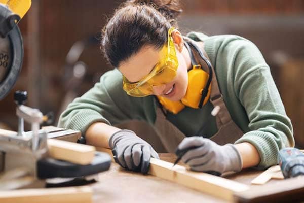 A female joiner marks a measurement on a batten of timber in a workshop.