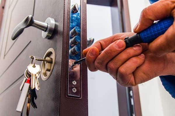 A locksmith using a screwdriver replacing a lock in a door. 