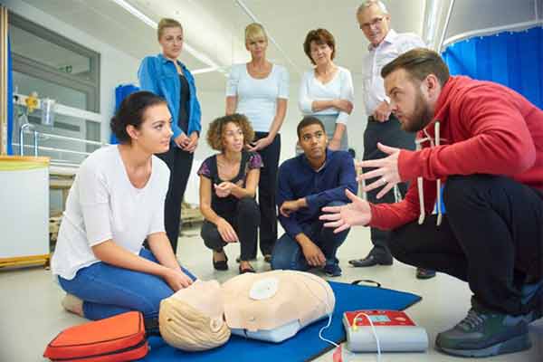 a first aid instructor teaching a class about resuscitation using a defibrillator