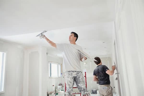 A self-employed plasterer and his apprentice plastering a ceiling.