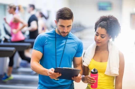 A personal trainer with a client in a busy gym