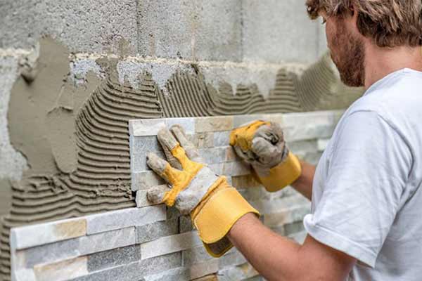 Tiler applying tiles to a breeze block wall.