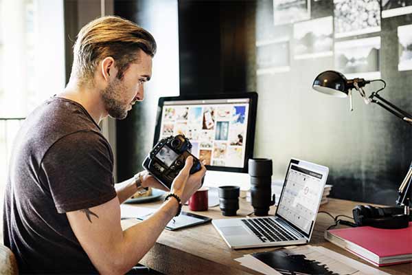 A photographer sat at his desk holding his camera going through pictures.